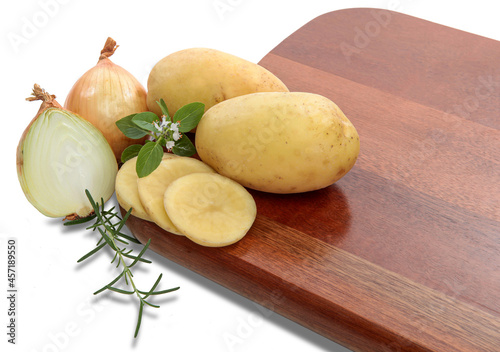 Ingredientes, batatas, cebolas, folhas de manjericão e alecrim em tábua de madeira no fundo branco para recorte.