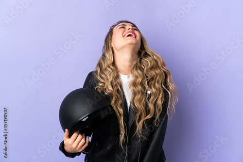 Young Brazilian woman holding a motorcycle helmet isolated on purple background laughing