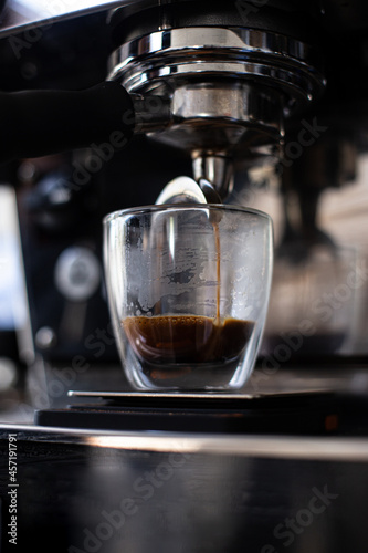 Сoffee machine makes double espresso in glass, close-up of coffee preparation, drops fall in a cup.