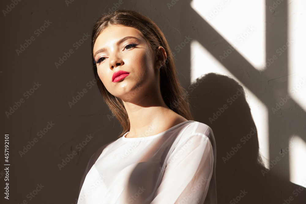 Young energy woman with a shadow pattern on body. Sun shining on wall.