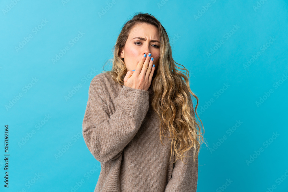 Young Brazilian woman isolated on blue background yawning and covering wide open mouth with hand Young Brazilian woman isolated on blue background yawning and covering wide open mouth with hand