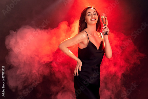 Excited young brunette woman in black dress holds glass of champagne. Party time. Holiday concept