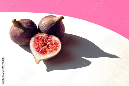 Autumn colors. Purple and magenta fig fruits on vibrant fuchsia and white geometric layered paper. Natural wattle wreath. Direct sunlight, long shadows.Simple minimal arrangement. Brilliant fall color photo