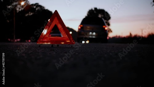 A failed car stands on the side of the road at night with the alarm on. An emergency stop sign standing on the road behind the car.