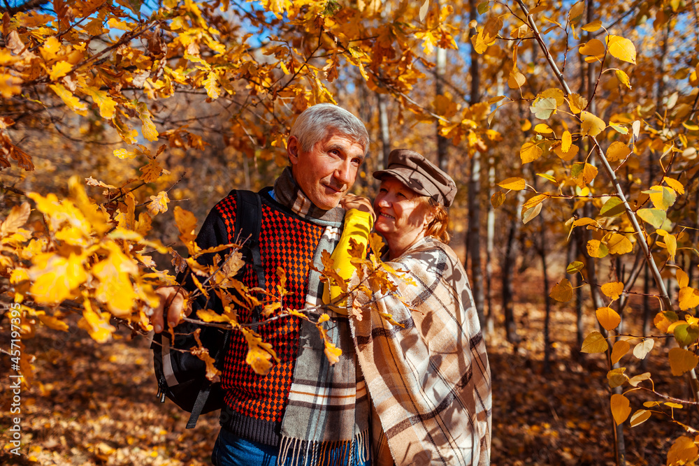 Fall season. Senior couple walking in autumn park. Middle-aged man and woman hugging and relaxing outdoors