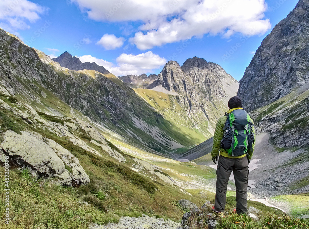 Active tourist with backpack standing at valley with rocky mountains background Active tourist with backpack standing at valley with rocky mountains background