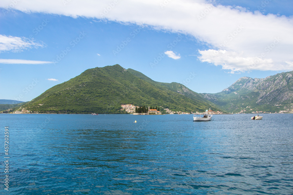 Boats at sea in the Bay of Kotor. In the background are two islands and mountains that rise above the blue sea.