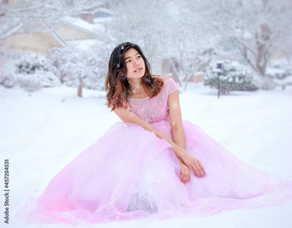 Teen girl in pink formal gown sitting outdoors in snow Teen girl in pink formal gown sitting outdoors in snow