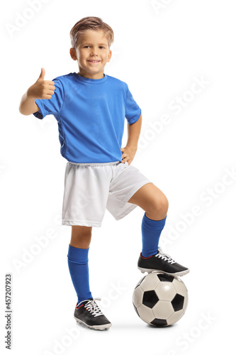 Cute little boy in a sports jersey stepping on a soccer ball and gesturing thumbs up