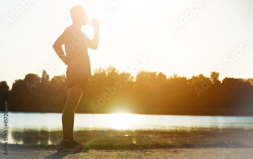 Runner drinks water while jogging in the park.