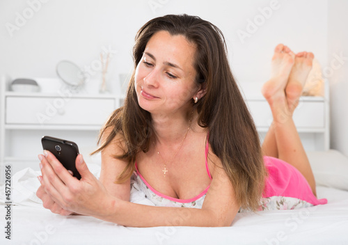 Portrait of young sexy woman using smartphone in bed at home photo