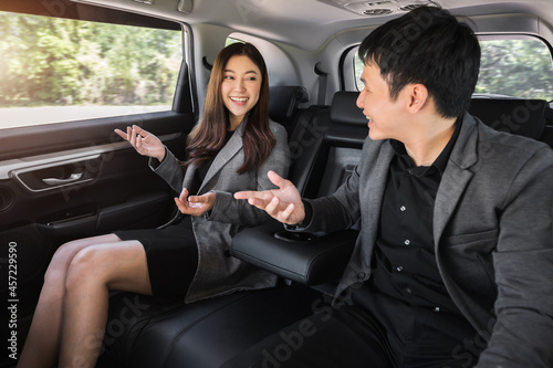 two happy business man and woman talking while sitting at the back seat of a car