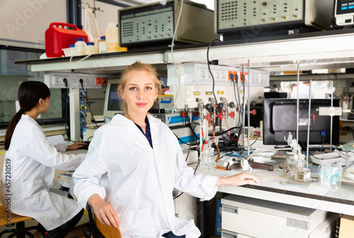 Portrait of glad cheerful smiling young female scientist near laboratory equipment at biochemical lab