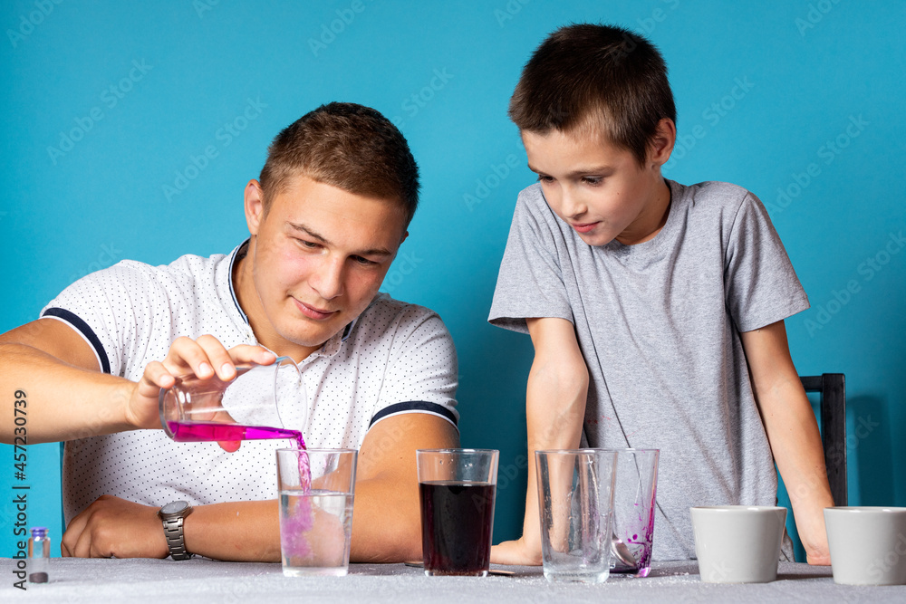 Chemistry education and training concept. Close-up of a boy and his dad, scientists pour potassium permanganate into a test tube for an experiment with a change of colors, experiments at home Chemistry education and training concept. Close-up of a boy and his dad, scientists pour potassium permanganate into a test tube for an experiment with a change of colors, experiments at home