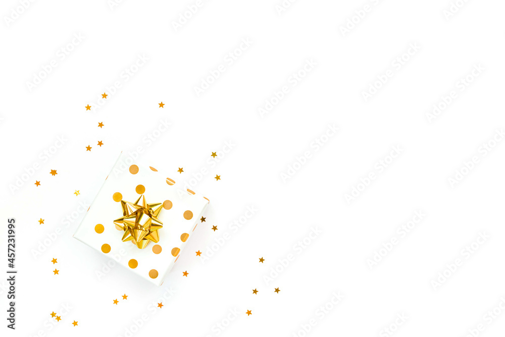 Top view of a golden dotted gift box and star shaped golden confetti on a white background. Copy space.