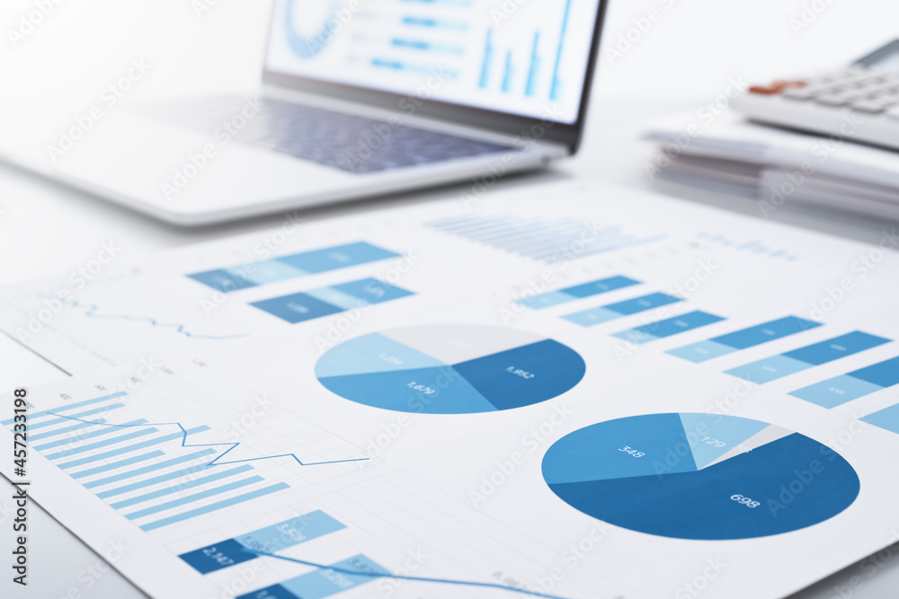 Business intelligence and analysis reports. Many graphs on reports and laptop display. Business intelligence and analysis reports. Many graphs on reports and laptop display.