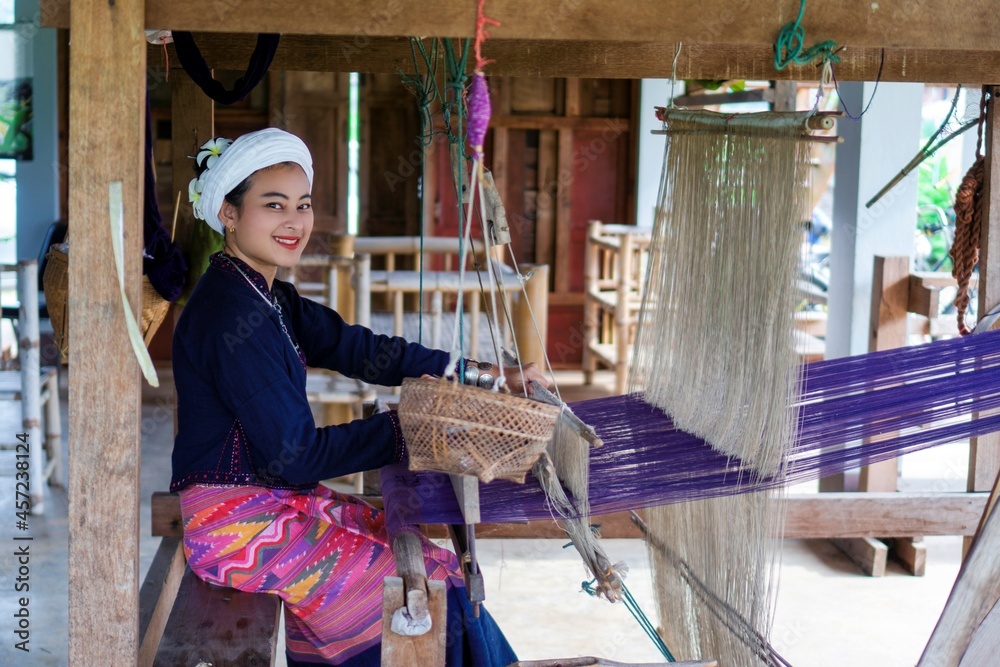 smile Asian woman in Tai Lue traditional dress (northern Thailand culture) weaving fabric with old wooden machine