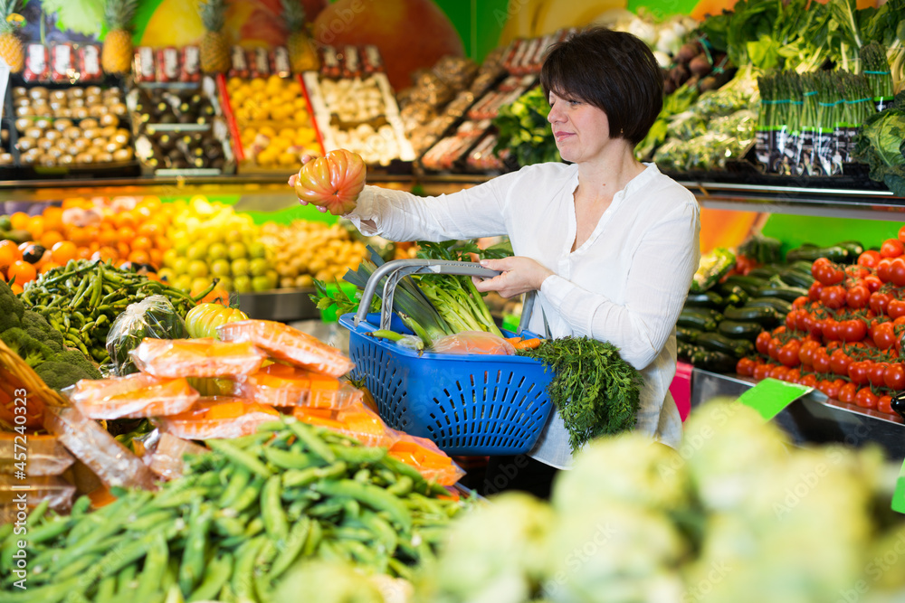 Mature woman buying fresh vegetables with basket on the market