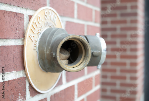 Auto sprinkler standpipe connector with missing cap and junk inside. Shows the importance of keeping the fire department connection covered. Outside of a building on brick wall. Selective focus.