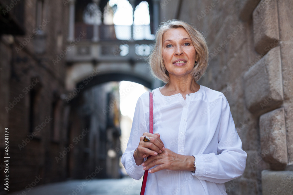 Elegant mature woman is posing in time walking on the street of old city. High quality photo