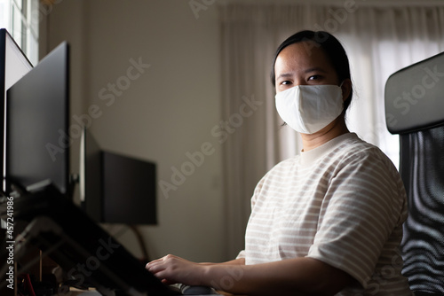 Asian woman with protection mask is working at home looking at camera 