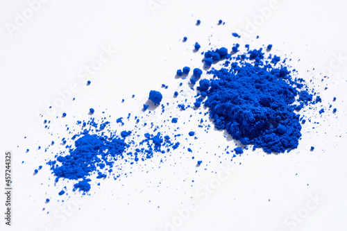 Close up of a large and a small portion of ultramarine, cobalt or indigo blue pigment isolated on white. The pigment was mixed with linseed oil to make oil paint. Narrow depth of field