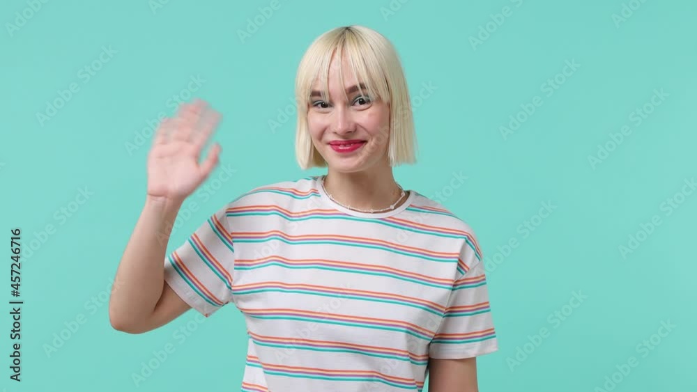 Fun young blonde short haircut woman 20s wears striped t-shirt look around for friend find waving meet greet with hand as notices someone isolated on pastel plain light blue background studio portrait Fun young blonde short haircut woman 20s wears striped t-shirt look around for friend find waving meet greet with hand as notices someone isolated on pastel plain light blue background studio portrait