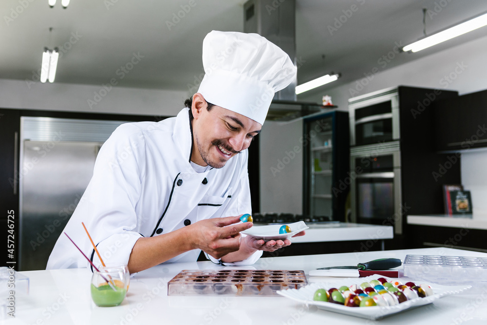 young latin man chocolatier in chef hat standing with chocolates candies on plate in a commercial kitchen in Mexico Latin America young latin man chocolatier in chef hat standing with chocolates candies on plate in a commercial kitchen in Mexico Latin America