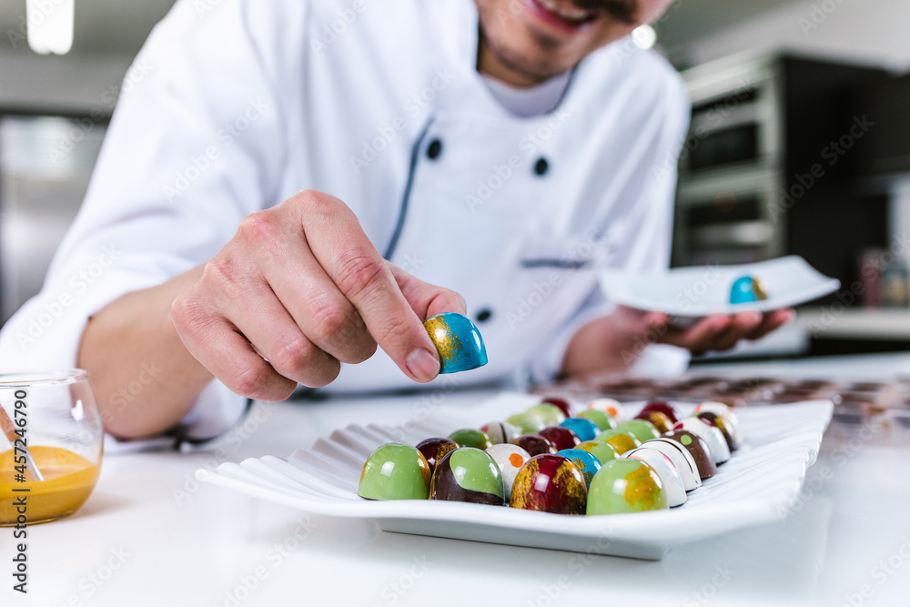 young latin man chocolatier in chef hat standing with chocolates candies on plate in a commercial kitchen in Mexico Latin America young latin man chocolatier in chef hat standing with chocolates candies on plate in a commercial kitchen in Mexico Latin America