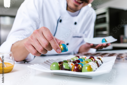 young latin man chocolatier in chef hat standing with chocolates candies on plate in a commercial kitchen in Mexico Latin America photo
