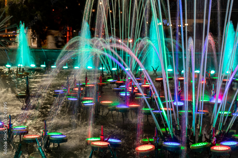 Abstract background, multicolored jets and splashes of water in a backlit fountain