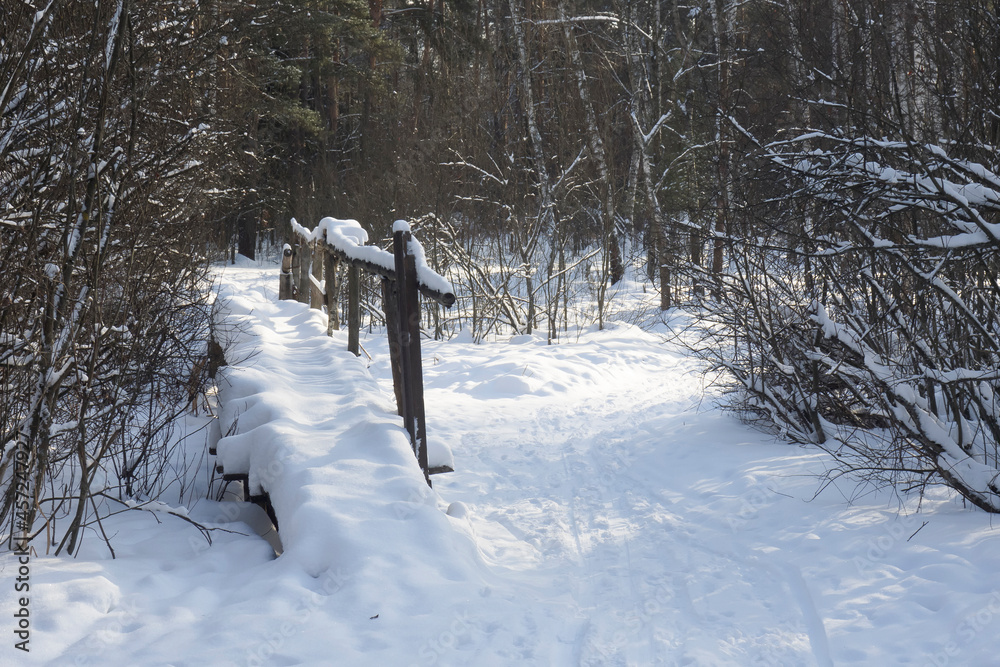 Old wooden footbridge over a stream under the snow in a winter park
