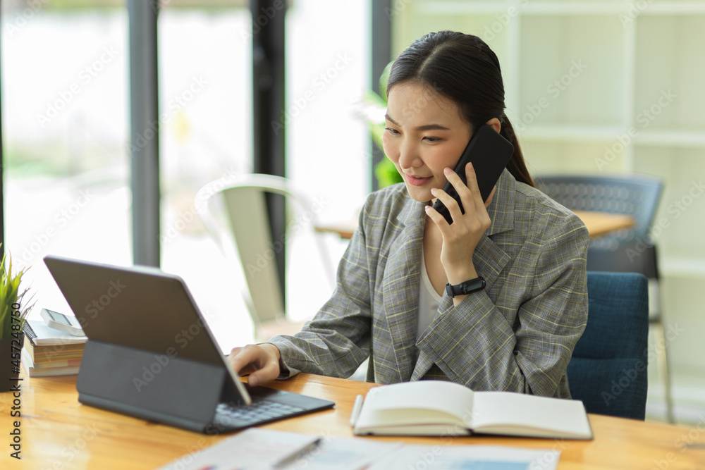 Asian businesswoman talking on mobile phone working on portable tablet in office Asian businesswoman talking on mobile phone working on portable tablet in office