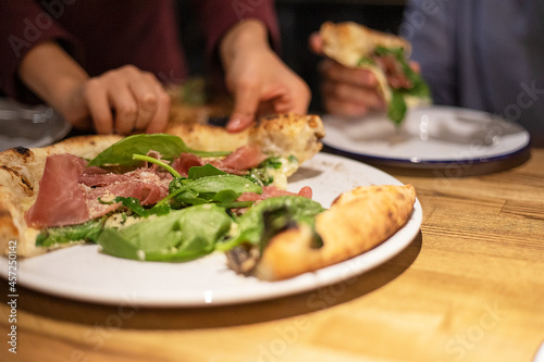 grabbing a hot pizza with prosciutto spinach and parmesan close-up, horizontal