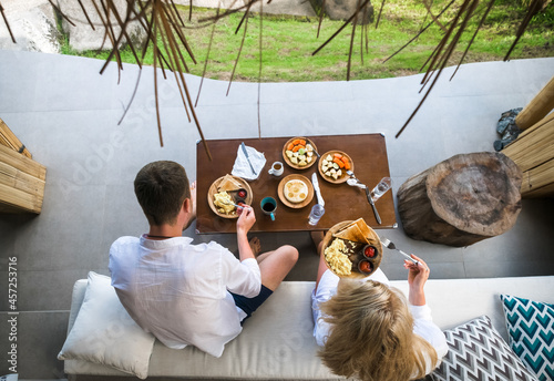 Young man and woman sitting at a table, in a villa with an open terrace, food in front of them, honeymoon. photo