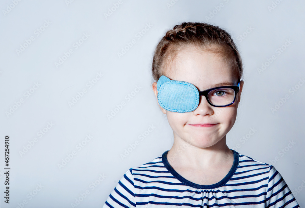 Child girl with an occluder on the eye in a striped jumper on a light background. Child girl with an occluder on the eye in a striped jumper on a light background.