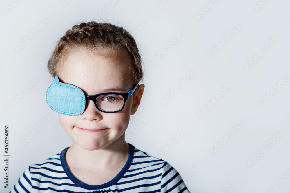 Child girl with an occluder on the eye in a striped jumper on a light background. Child girl with an occluder on the eye in a striped jumper on a light background.