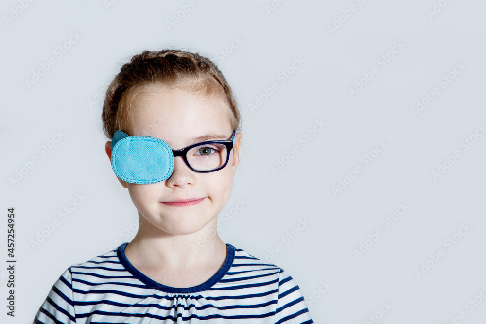 Child girl with an occluder on the eye in a striped jumper on a light background. Child girl with an occluder on the eye in a striped jumper on a light background.