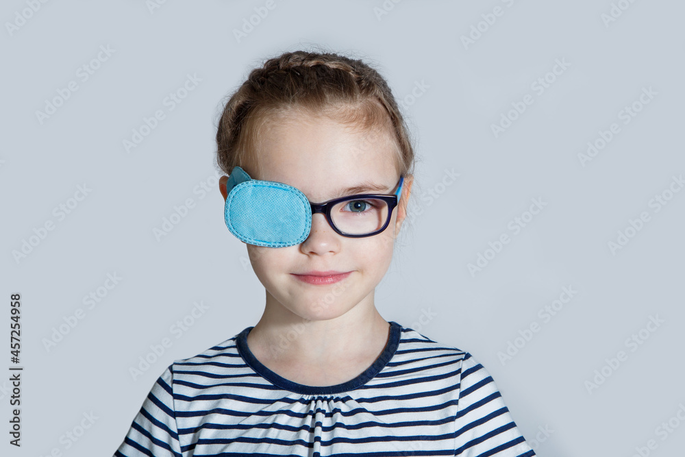 Child girl with an occluder on the eye in a striped jumper on a light background.