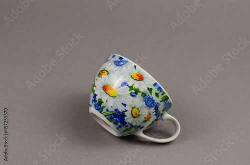 Minimalist composition with Ceramic teacup on gray background. Beautiful cup decorated with white and yellow daisies.