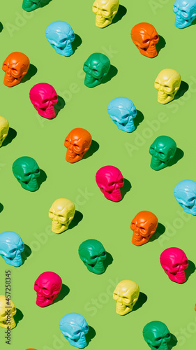 Creepy and spooky pattern of colorful human skulls isolated on a vivid neon green background. Creative Halloween or Day Of The Dead concept. Fashion retro future aesthetic. Flat lay.