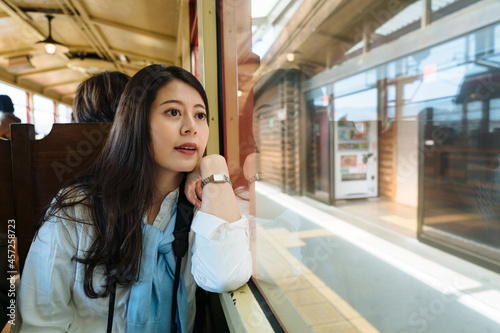 portrait of beautiful asian female visitor is looking at the station through the window while taking sagano romantic train in autumn in Arashiyama Kyoto, Japan. photo