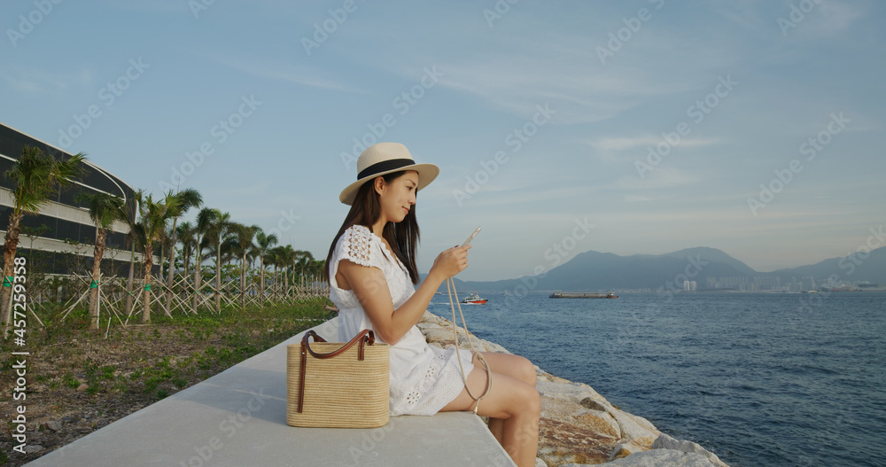 Travel woman sit beside the sea and use of mobile phone