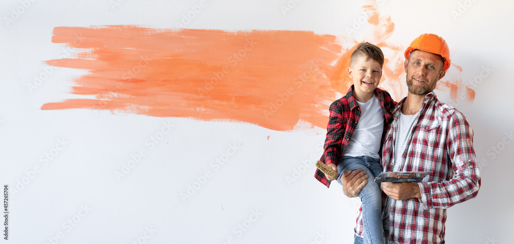 is renovating his house, the father is holding his son against the background of the wall with place for text. Father's day. Baner.
