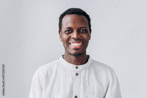 Portrait of handsome positive young African-American man in white shirt looking into camera on light grey background closeup