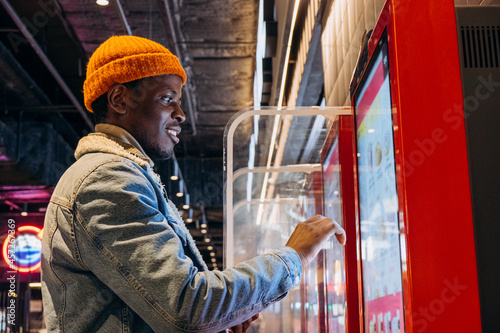 Fotografie Positive African-American guy in orange knitted hat with wireless earphones orde