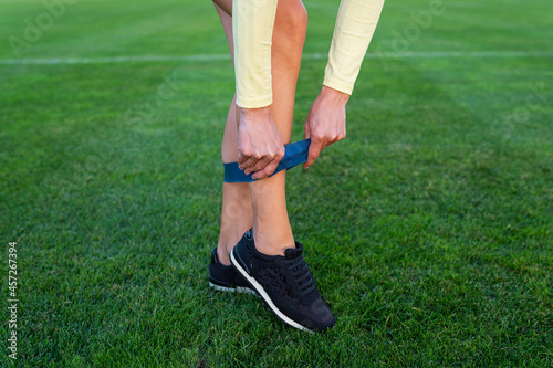 A girl in sneakers starts putting on a sports elastic band at the stadium for sports exercises. Sports and health concept.