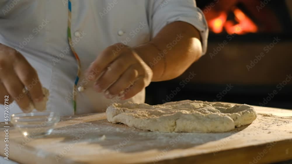A professional chef prepares pizza dough and adds yeast to it. Cooking white pizza and hot pizza in a wood-fired oven.