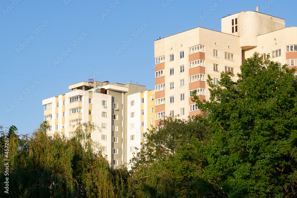 Tall buildings above dense green trees in the evening sunlight.