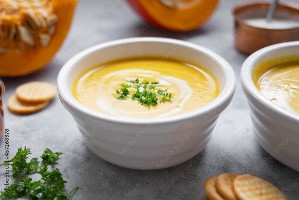 Pumpkin soup with coconut milk and squash slices. Creammy autumn soup in white bowl on gray background. Pumpkin soup with coconut milk and squash slices. Creammy autumn soup in white bowl on gray background.